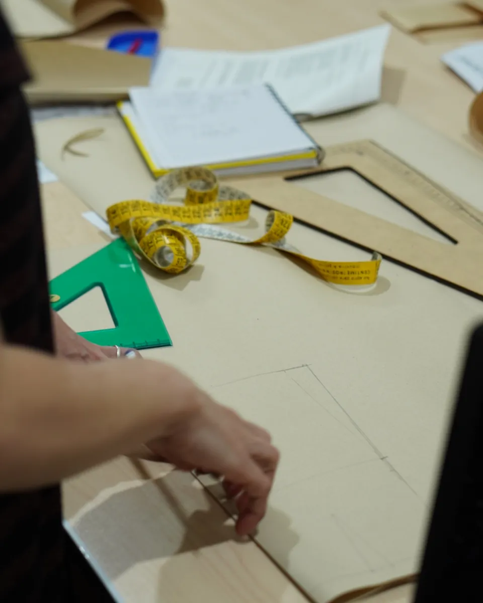 Manos de una alumna marcando un molde con escuadra en el taller de la escuela.