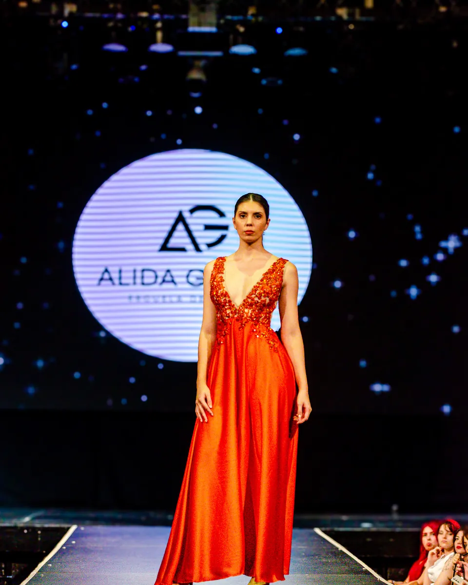 Alumna de la Escuela de Diseño Alida Gómez en la pasarela del desfile anual 2024, con un vestido naranja.